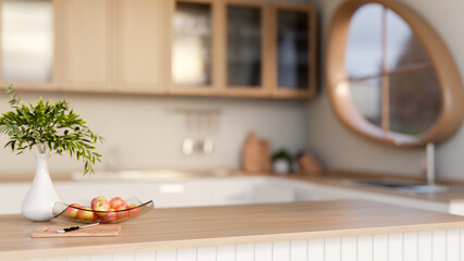 A knife on cutting board and apples on glass plate with flower vase on wooden top counter in kitchen