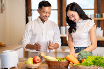 Asian man holding blender and watching woman cutting apples making smoothie drink at kitchen counter