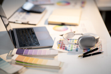 Laptop with headphones placing atop color charts or palette on working table in designer's office.
