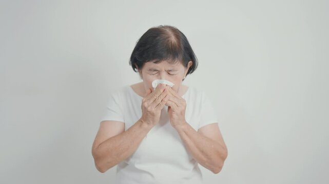 Elderly woman blowing her nose with tissue for concepts of Common Cold, Influenza, Flu, Hay, Fever, Covid 19, Respiratory Infection, Sinusitis, Allergic Rhinitis, Allergy, Medical and health care