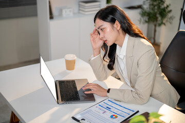 Businesswoman or office worker massaging temple getting headache as looking at laptop on her table.