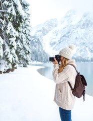 A woman in a warm jacket captures stunning photos of majestic snow-covered mountains, surrounded by a serene winter landscape under a clear blue sky.