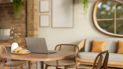 Laptop and breads on plate aside flower vase on wooden stool table in a bricks wall lounge or cafe.