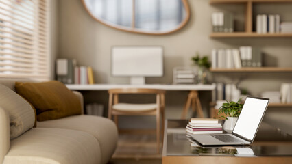 White screen laptop with books on glass top wooden table and fabric sofa in a bedroom or living room