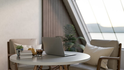 Laptop with coffee and breads aside books on white round table with armchair in living room or cafe.