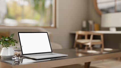 White screen laptop with books and coffee cup on glass top wooden table in a bedroom or living room.