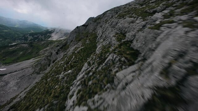 FPV drone skims rocky slope in Tauplitz before diving and revealing a valley with water and greenery.