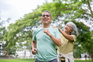Fototapeta premium Old woman massaging glasses man shoulder while he smiling and preparing to run on grass lawn in park