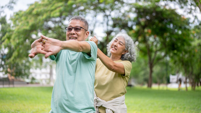 Old woman massaging glasses man shoulders while he standing and stretching on grass lawn in the park