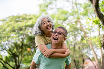 Fototapeta premium Glasses old man carrying a woman on his back as laughing together while standing or walking in park.