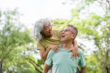 Fototapeta premium Glasses old man carrying old woman on his back and smiling at each other while standing in the park.