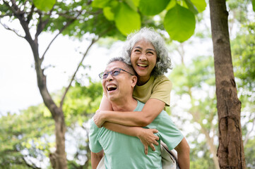 Glasses old man laughing as carrying smiling old woman on his back while standing or walking in park