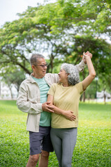 Fototapeta premium Glasses old man and old woman smiling and holding hands while dancing together on grass lawn in park