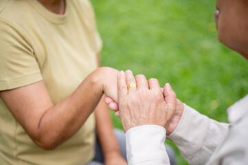 Close up of old man hand with gold wedding ring holding a woman hands while sitting together in park