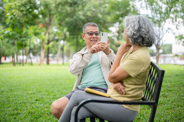Fototapeta premium Glasses old man holding smartphone taking picture of a woman while sitting together on bench in park