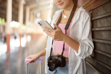 Close up of woman looking at phone holding luggage standing aside carriage at train station platform