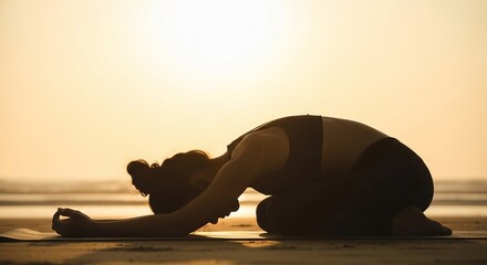 Silhouette of woman in child's pose on beach at sunset, yoga practice