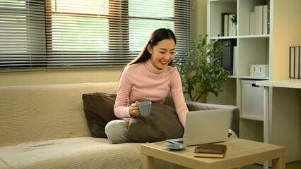 A Cheerful woman working from home in a bright living room, combining productivity and relaxation...