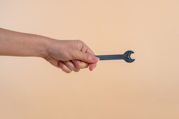 Hand holding a wrench isolated on cream background.