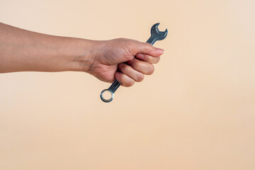Hand holding a wrench isolated on cream background.