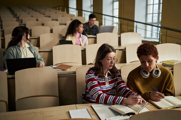 Group of multiethnic university students sitting in lecture hall working on assignments, young...