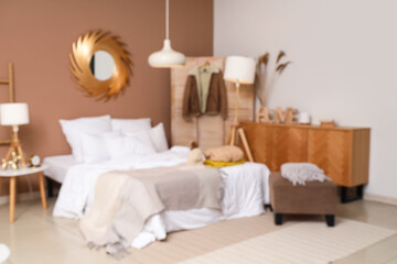 Blurred view of cozy bedroom with winter clothes on bed and lamps
