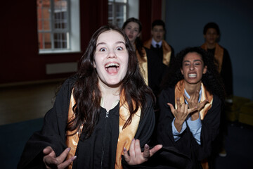 Caucasian teenage girl and multiethnic group of classmates wearing graduation gowns celebrating and...