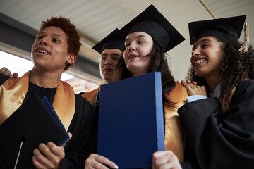 Diverse group of young university students wearing graduation caps and gowns standing together...