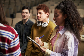 Group of multiethnic university students interacting during class, young Black woman taking notes...