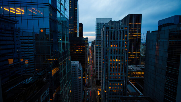 New York City's urban skyline at night features towering glass skyscrapers and illuminated office buildings reflecting the blue sky