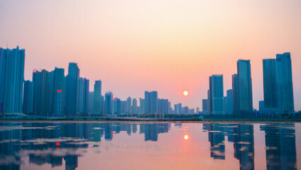 Fototapeta premium Shanghai's urban skyline glows at sunset, with modern architecture reflecting on the water as night approaches