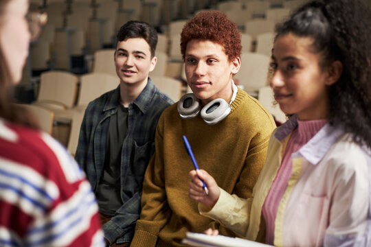 Group of multiethnic university students including Caucasian teenage boy, Black male and female classmates listening attentively to instructor and taking notes during classroom discussion