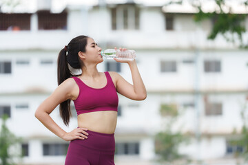 Young asian sportswoman drinking water after training outdoors