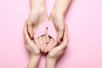 Hands of woman and child with paper lungs on pink background