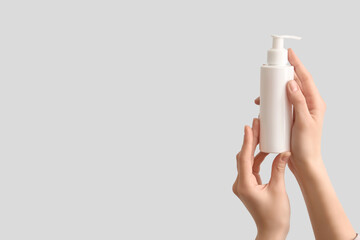 Female hands with bottle of natural cream on grey background, closeup