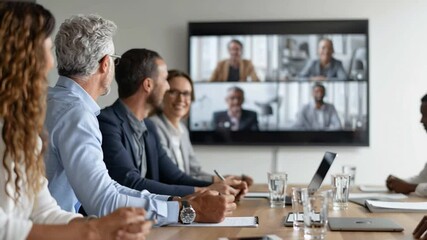 team gathered in conference room with screen showing remote colleagues on video call - Powered by Adobe