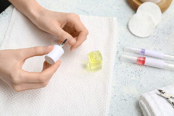 Female hands with bottle of cuticle oil and towel on light background