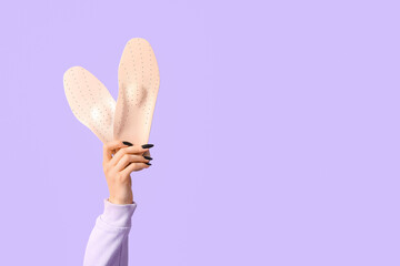 Female hands holding orthopedic insoles on lilac background