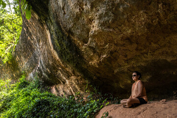Woman meditating in a natural cave. Serene scene with rock formations and lush greenery.