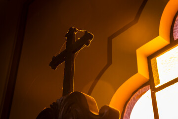 Wooden cross with intricate details bathed in dim light inside a Catholic church in Brazil. Evokes...
