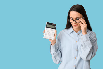 Beautiful young woman with calculator on blue background