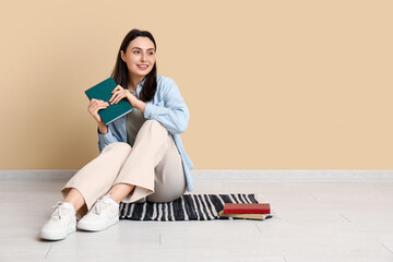 Young woman sitting on floor with book near beige wall