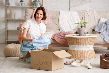 Young pretty woman packing clothes in donation cardboard box at home