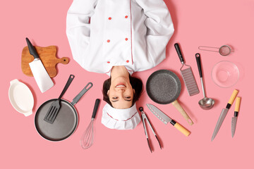 Happy young female cook with different kitchen utensils lying on pink background