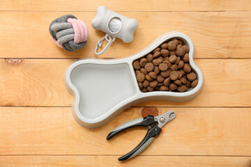 Bone shaped bowl with dry pet food near chew toy and pet nail clippers on wooden background