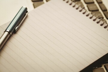 Flat design is showing spiral-bound notebook angled on laptop keys, metal pen adding workspace vibe