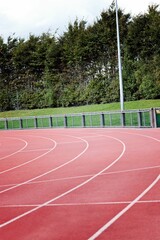 Curved red track is winding in flat design with white lanes, railing, hedge and light pole