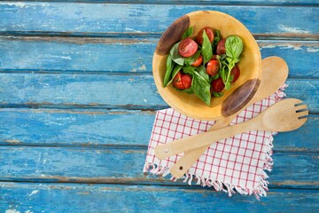 Fresh salad in wooden bowl by spoon and fork on table