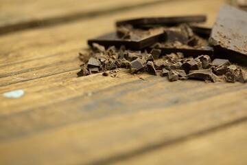 Dark chocolate shards, bar segments and crumbs are being shown on wooden table surface, flat design