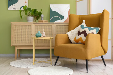 Armchair with cushions, chest of drawers with plant and folding screen in interior of living room